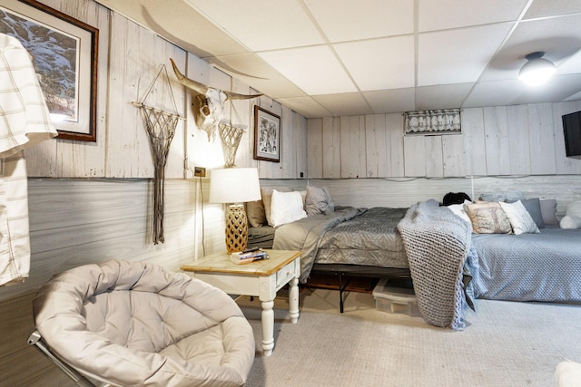 carpeted bedroom featuring wooden walls and a drop ceiling