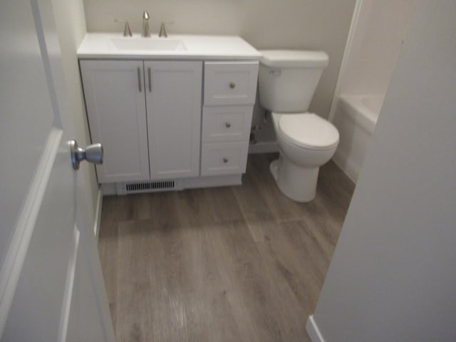 bathroom with hardwood / wood-style floors, vanity, toilet, and a tub to relax in