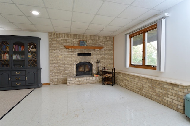 unfurnished living room with a paneled ceiling, a fireplace, and brick wall