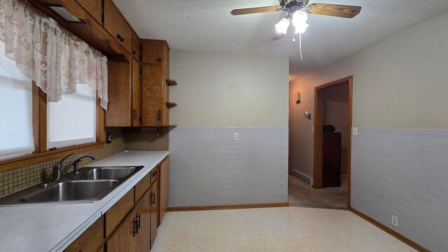 kitchen featuring a textured ceiling, tile walls, ceiling fan, and sink