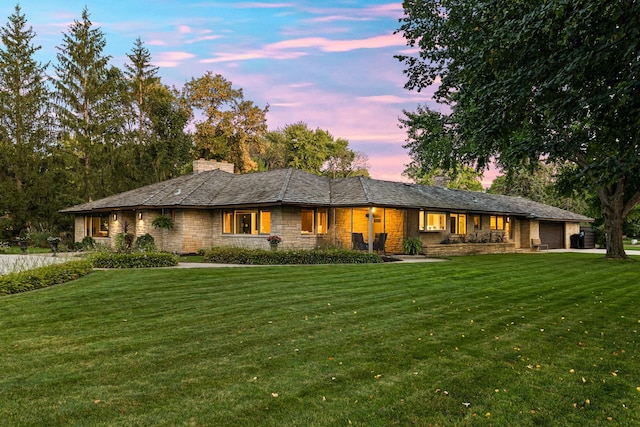 view of front of home with a garage, stone siding, a yard, and a chimney