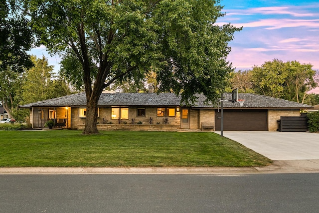 view of front of property featuring a garage, stone siding, driveway, and a front lawn