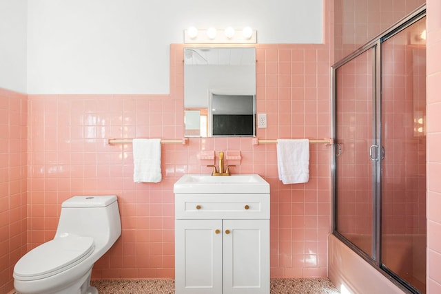 bathroom featuring tile walls, toilet, shower / bath combination with glass door, vanity, and speckled floor