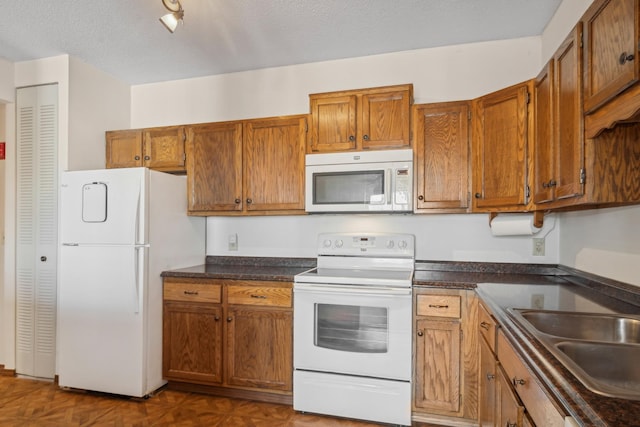 kitchen with a textured ceiling, dark parquet flooring, sink, and white appliances