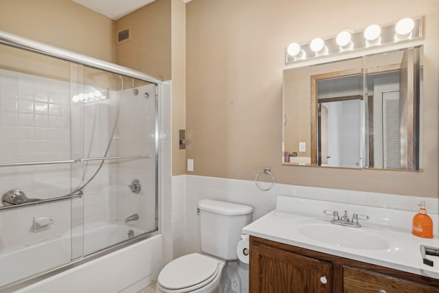 full bathroom featuring tile walls, vanity, toilet, and combined bath / shower with glass door