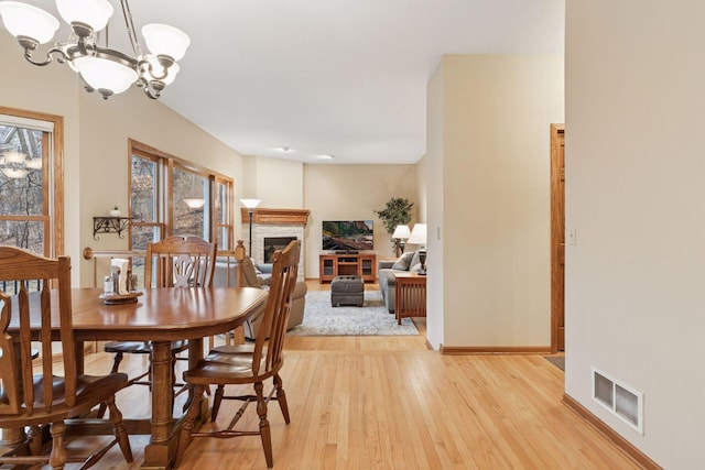 dining space featuring baseboards, visible vents, a fireplace, light wood-type flooring, and a chandelier