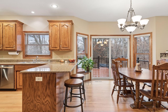 kitchen featuring a notable chandelier, light wood-style flooring, a sink, a kitchen breakfast bar, and dishwasher