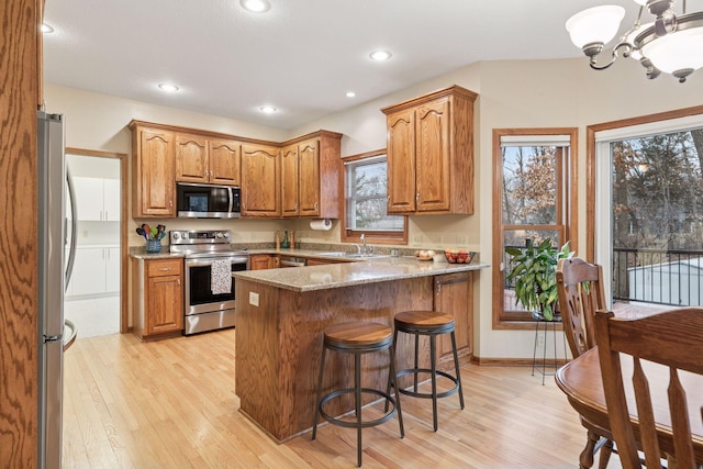 kitchen with a notable chandelier, stainless steel appliances, light wood-style floors, a peninsula, and brown cabinetry