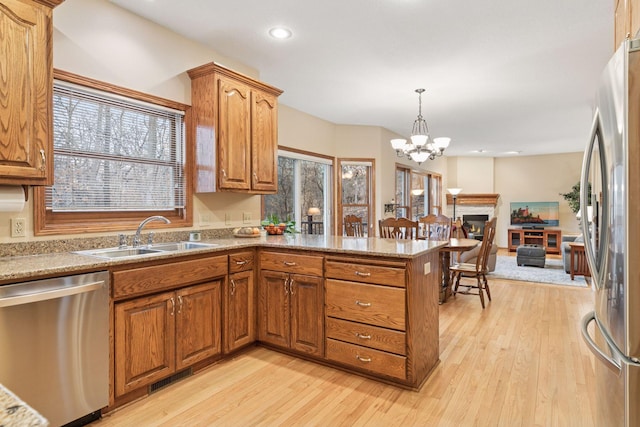 kitchen featuring a sink, light wood-style floors, appliances with stainless steel finishes, a peninsula, and brown cabinetry