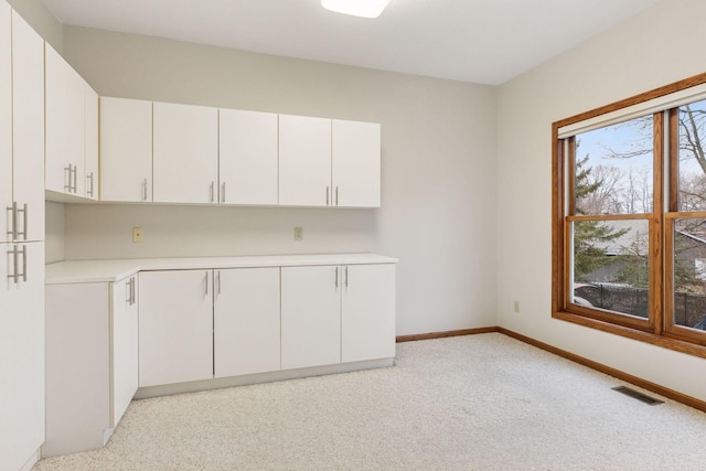 kitchen with baseboards, visible vents, light countertops, light carpet, and white cabinetry