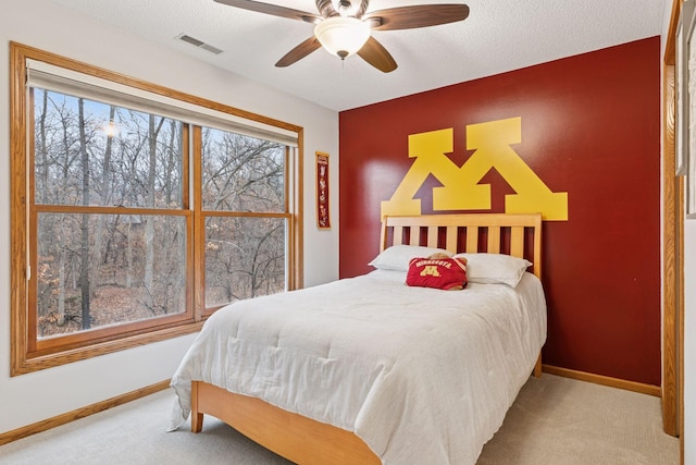 carpeted bedroom with an accent wall, baseboards, visible vents, and a textured ceiling