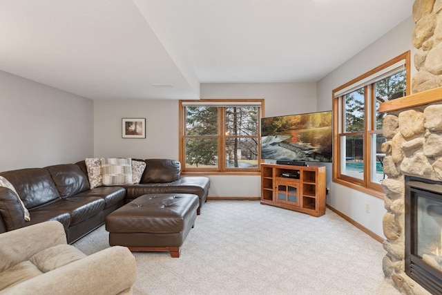 carpeted living area with a stone fireplace and baseboards