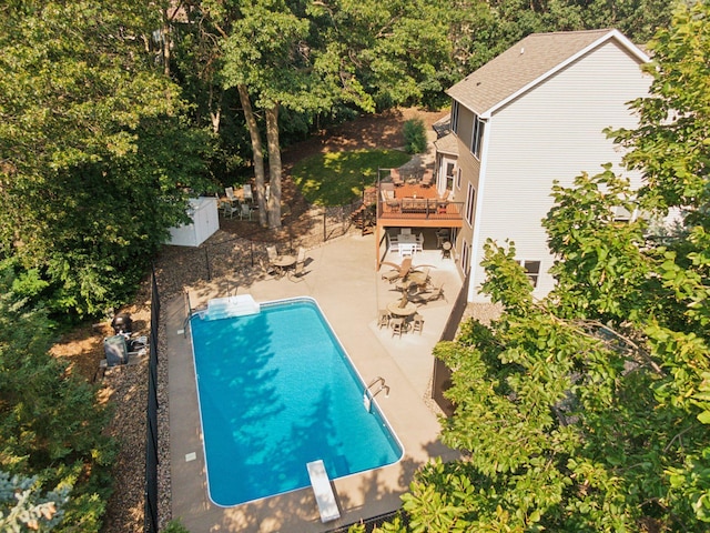 pool with a diving board, a wooden deck, and a patio area