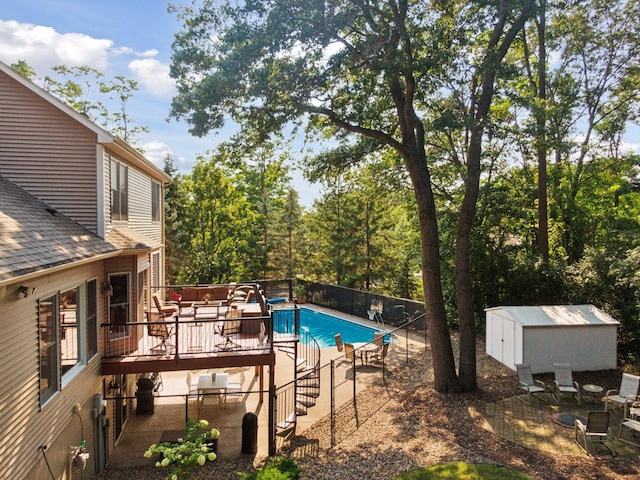 view of pool with a fenced in pool, fence, a shed, a wooden deck, and an outbuilding