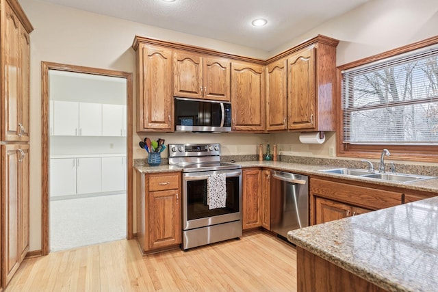 kitchen with brown cabinetry, stainless steel appliances, light wood-type flooring, and a sink