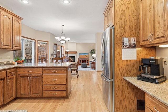 kitchen with light wood finished floors, brown cabinets, a peninsula, freestanding refrigerator, and a notable chandelier