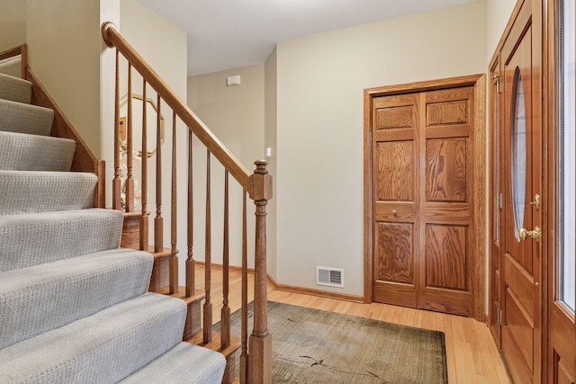 foyer with stairway, light wood-style flooring, visible vents, and baseboards