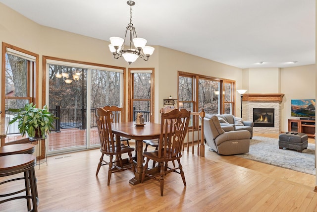 dining area with visible vents, light wood-type flooring, a stone fireplace, and an inviting chandelier