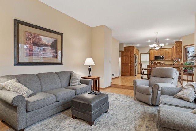 living room with an inviting chandelier, light wood-style floors, and baseboards