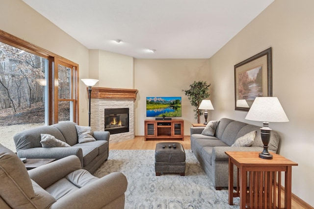 living area with baseboards, a stone fireplace, and light wood finished floors