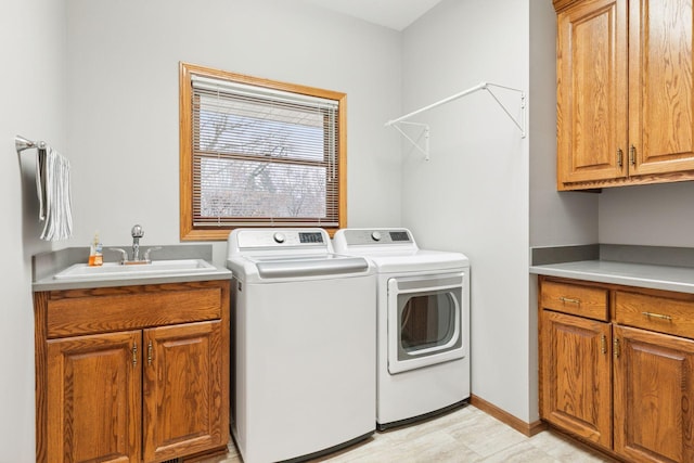 laundry room with cabinet space, washer and dryer, baseboards, and a sink