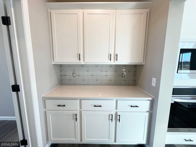 bar with white cabinetry, dark wood-type flooring, tasteful backsplash, light stone counters, and appliances with stainless steel finishes