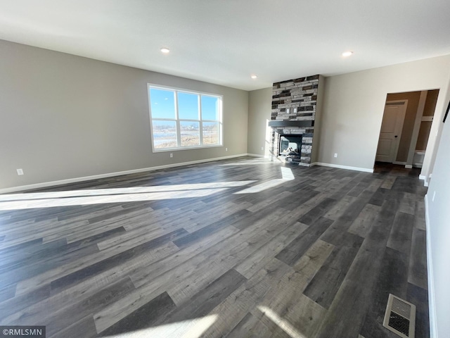 unfurnished living room featuring a stone fireplace and dark hardwood / wood-style flooring