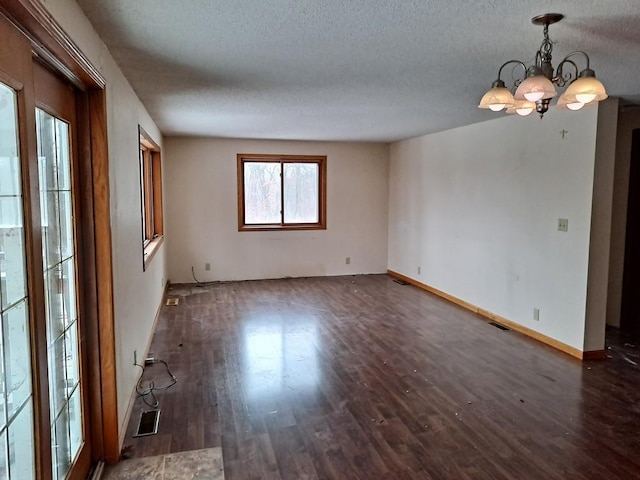 unfurnished room featuring dark hardwood / wood-style flooring, a textured ceiling, and a notable chandelier