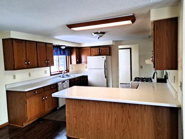 kitchen featuring sink, white appliances, kitchen peninsula, and dark wood-type flooring