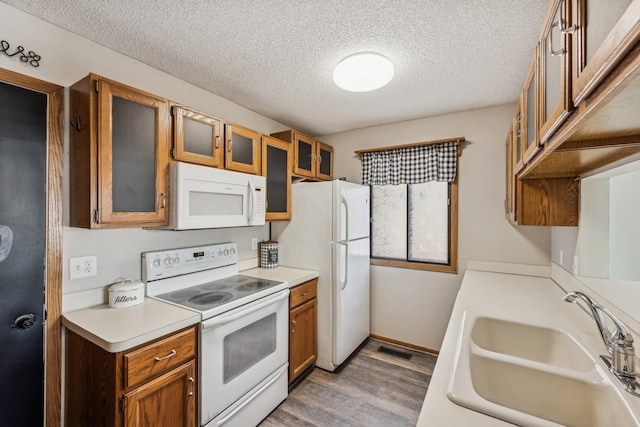 kitchen with sink, white appliances, a textured ceiling, and light wood-type flooring