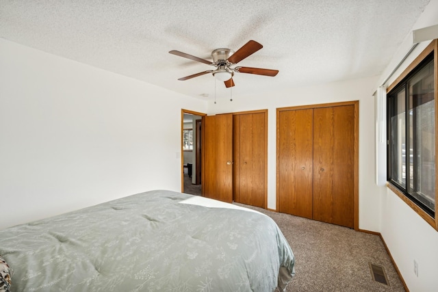 bedroom with ceiling fan, carpet flooring, a textured ceiling, and two closets