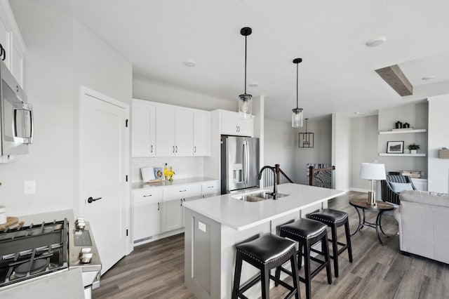 kitchen with hanging light fixtures, stainless steel appliances, a kitchen island with sink, and dark wood-type flooring