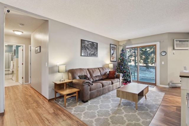 living room featuring a baseboard heating unit, a wall mounted AC, a textured ceiling, and light hardwood / wood-style floors