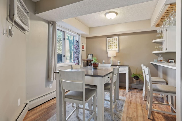 dining room with light hardwood / wood-style floors, a wall mounted AC, a textured ceiling, and baseboard heating