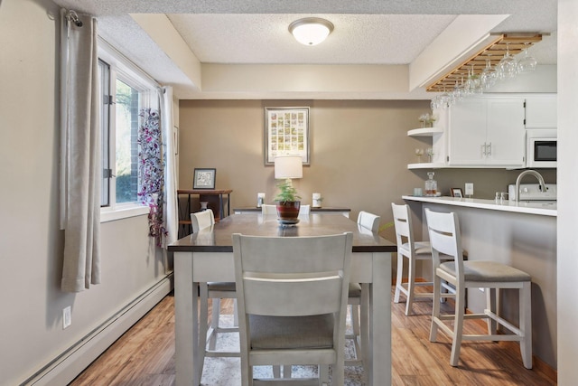 dining space with a healthy amount of sunlight, a textured ceiling, baseboard heating, and light hardwood / wood-style flooring