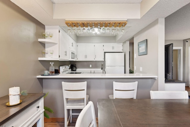 kitchen featuring white cabinetry, white appliances, kitchen peninsula, and a breakfast bar area