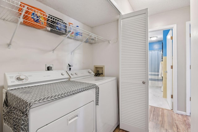 laundry area with washing machine and dryer, a textured ceiling, and light wood-type flooring