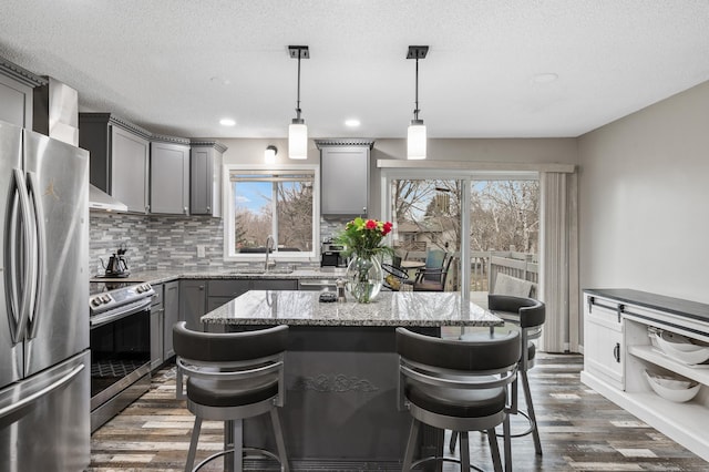 kitchen with gray cabinetry, dark hardwood / wood-style floors, a kitchen island, a kitchen bar, and stainless steel appliances