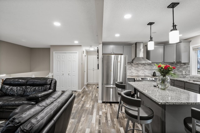 kitchen with stainless steel appliances, wall chimney range hood, hardwood / wood-style floors, a kitchen island, and hanging light fixtures