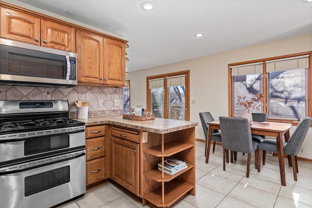 kitchen with backsplash, stainless steel appliances, kitchen peninsula, and light tile patterned flooring