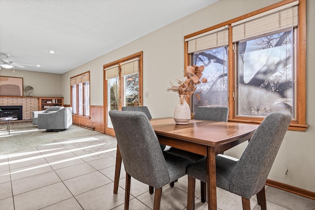 tiled dining area featuring ceiling fan and a brick fireplace