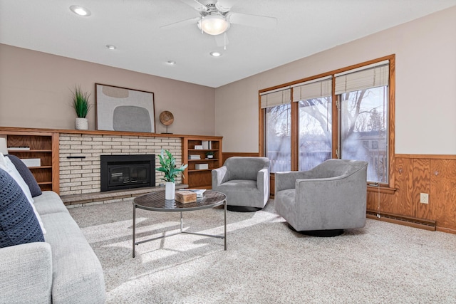 carpeted living room with baseboard heating, ceiling fan, a fireplace, and wood walls