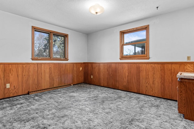 empty room with wooden walls, a baseboard heating unit, light colored carpet, and a textured ceiling