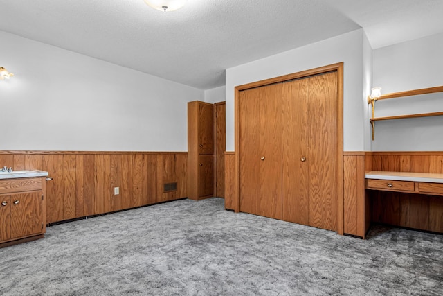 unfurnished bedroom with light carpet, a textured ceiling, wooden walls, and a closet