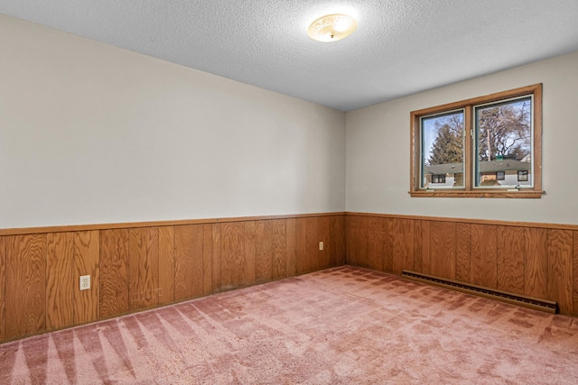 carpeted spare room featuring a baseboard heating unit, a textured ceiling, and wood walls