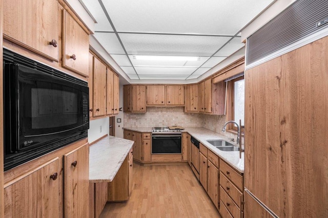 kitchen with decorative backsplash, light wood-type flooring, a drop ceiling, sink, and black appliances