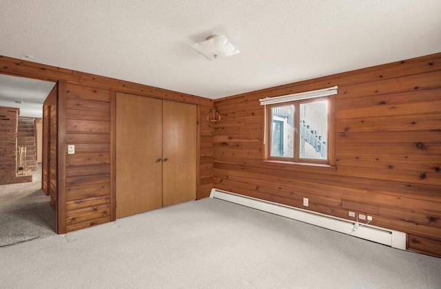 unfurnished bedroom with baseboard heating, wooden walls, a closet, and carpet