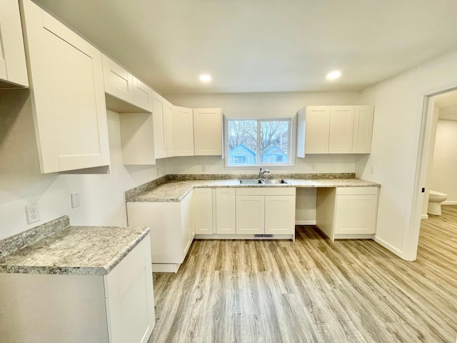 kitchen featuring white cabinets, light wood-type flooring, light stone countertops, and sink