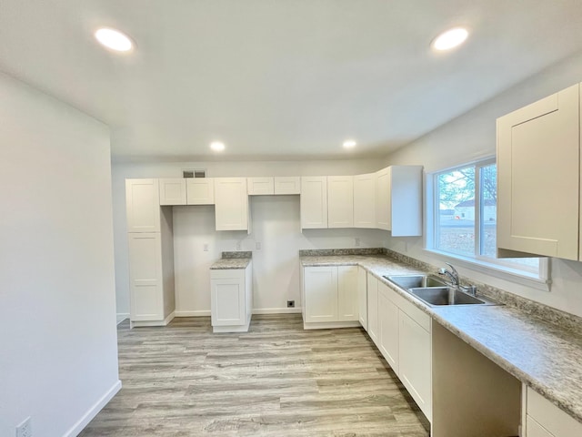 kitchen with light wood-type flooring, white cabinetry, and sink