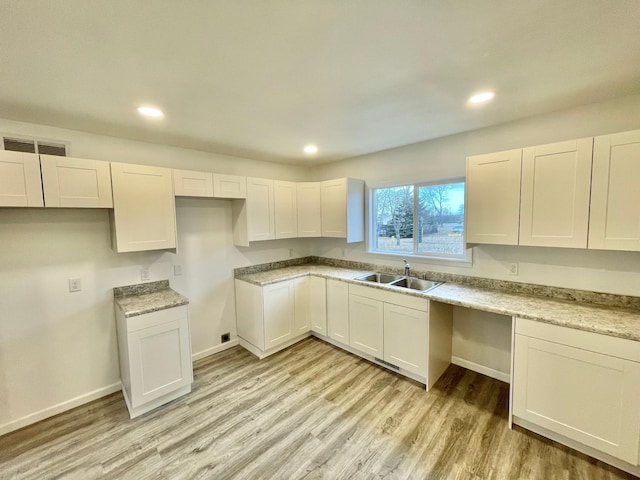 kitchen with white cabinetry, sink, light stone countertops, and light wood-type flooring